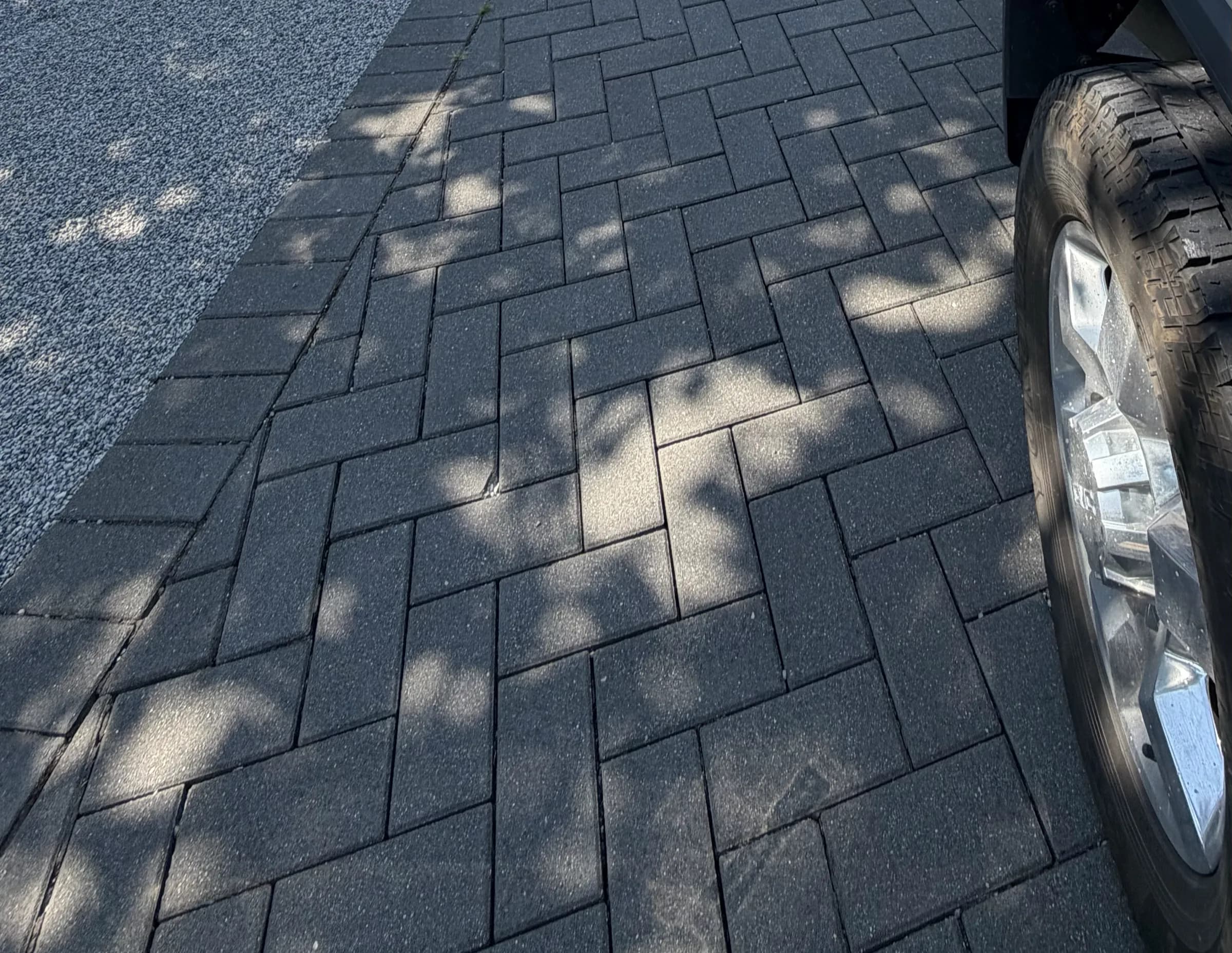 Herringbone driveway pavers in dappled shade, the joints open and the sand gone