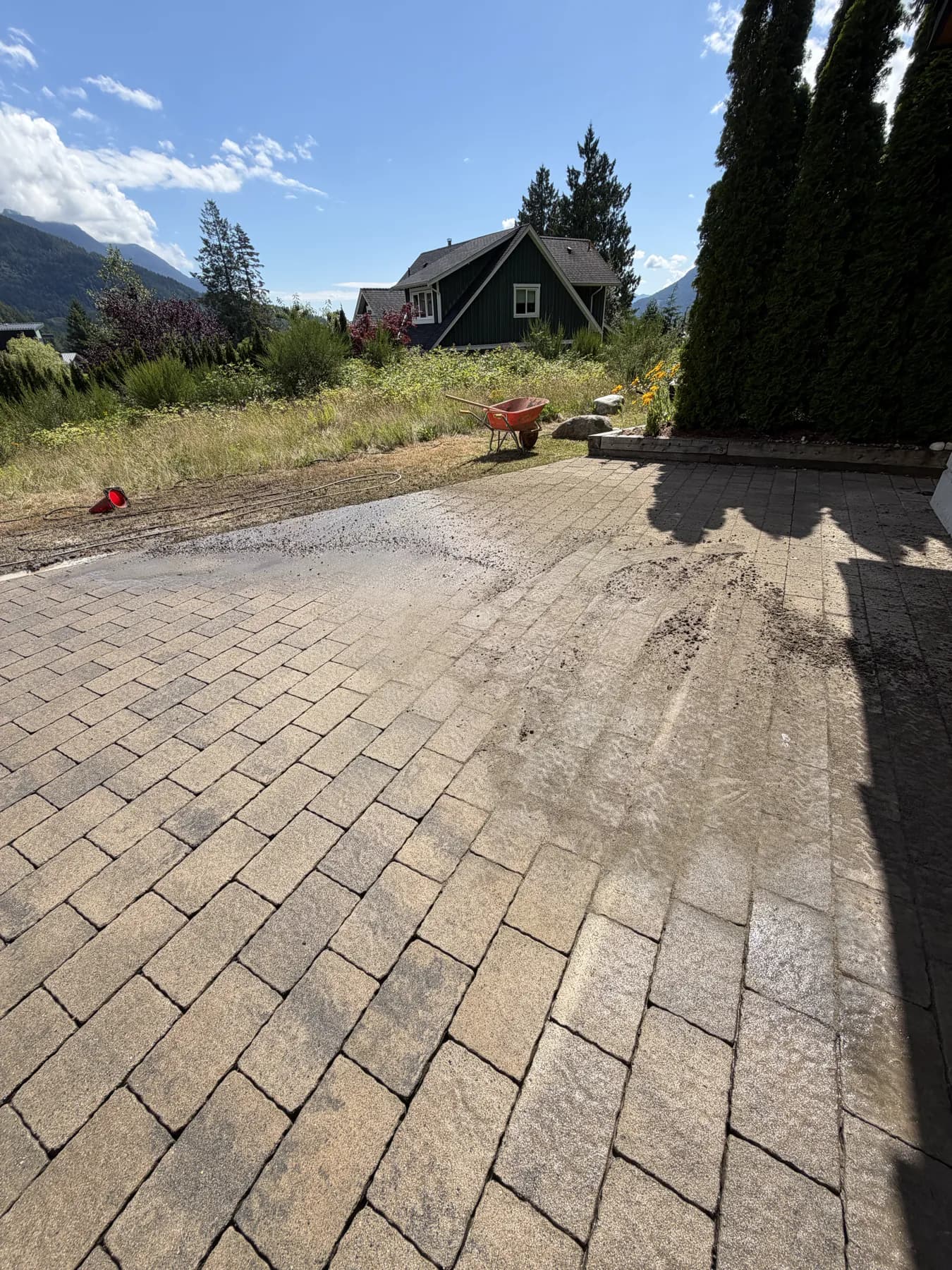A paver driveway part-way through cleaning, the washed section meeting the untouched one